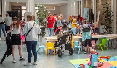 A busy indoor scene  of children and families drawing at a table in a gallery