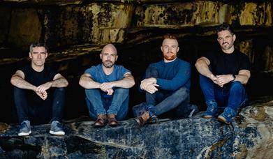 4 male band memebers sit in cave like surroundings