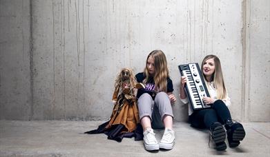 image of vokxen sitting on the ground with one member of the band holdinf a puppet of a witch.