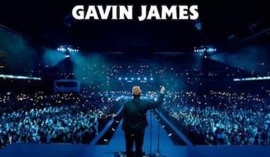 Gavin James facing a full arena, phone torches shining, blue mood lighting. White text above states 'Gavin James'.