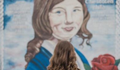 A woman stands before a striking mural of Julie Livingstone, emphasizing the connection between the viewer and the artwork.