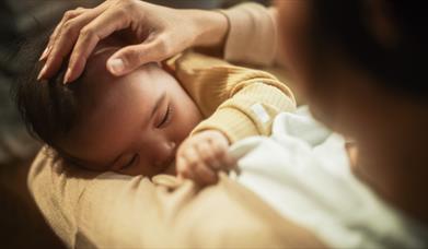 A mother looks down on her baby in her arms as she breastfeeds them.