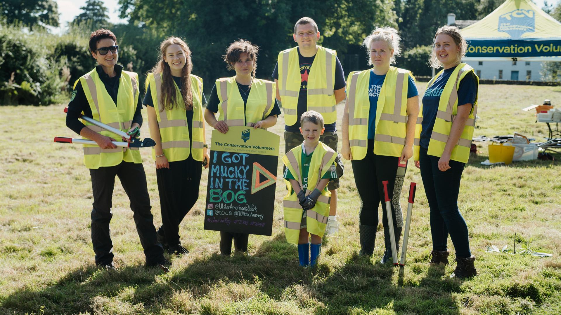 A group pic of 7 Attendees from last year's bogging event holding a sign saying I got mucky in the Bog.