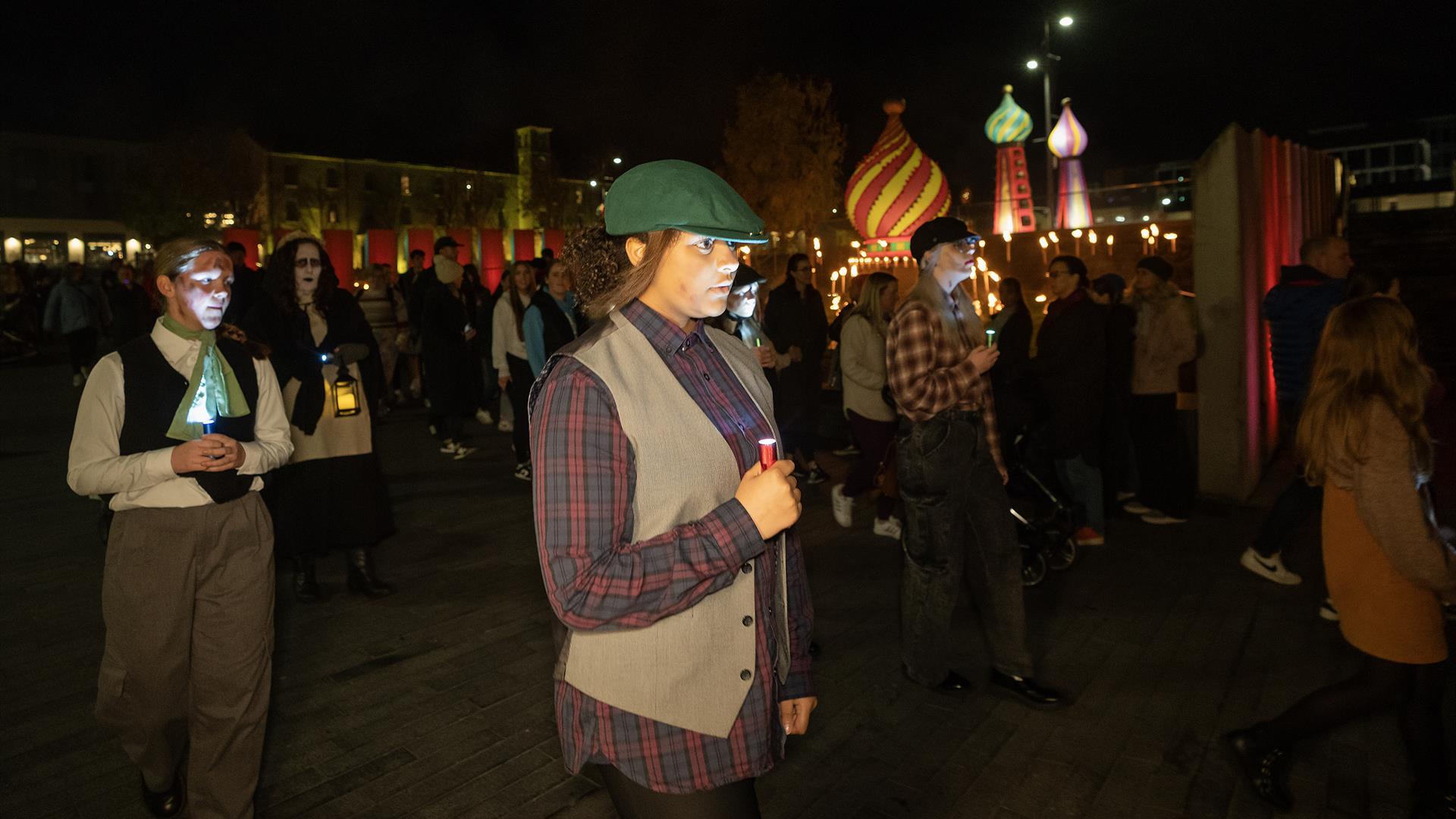 young girl dressed in old style clothing walking with a candle or light.