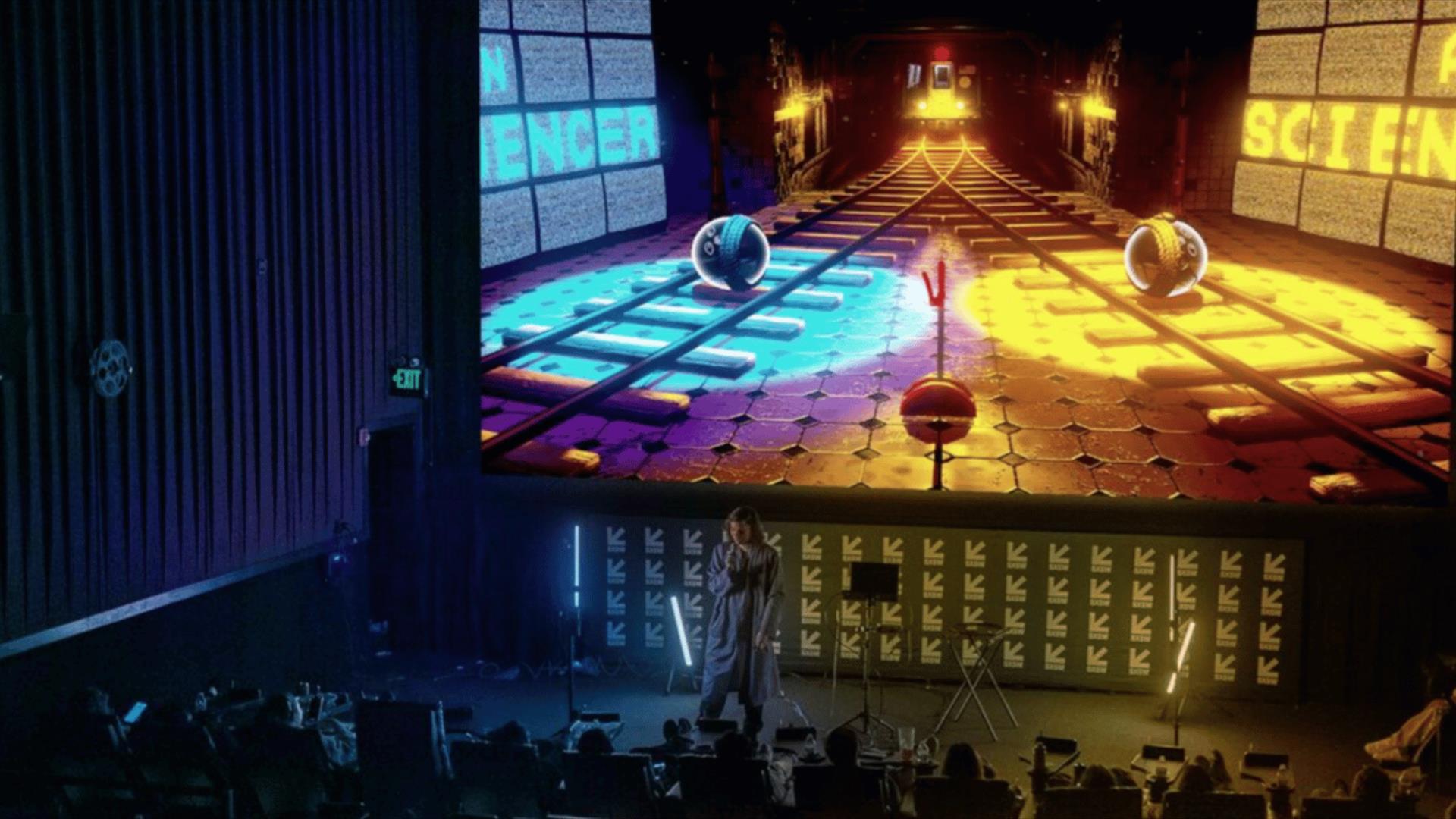 Large theater stage with an audience facing a big screen showing a colorful sci‑fi corridor with glowing lights and floating spheres, including "SCIEN