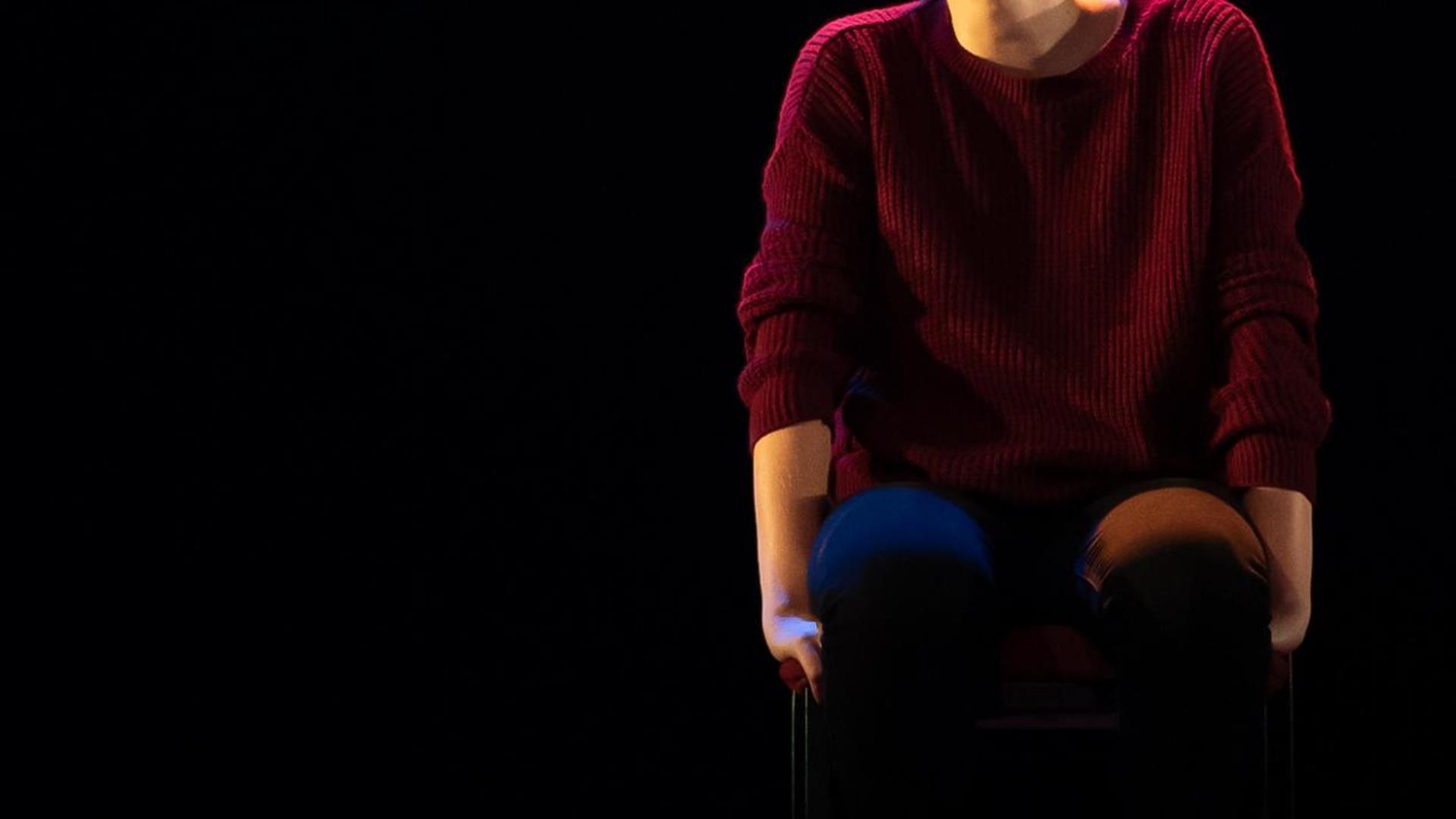 Phoebe Waller-Bridge sits on stool smiling towards audience wearing burgundy jumper and Jeams