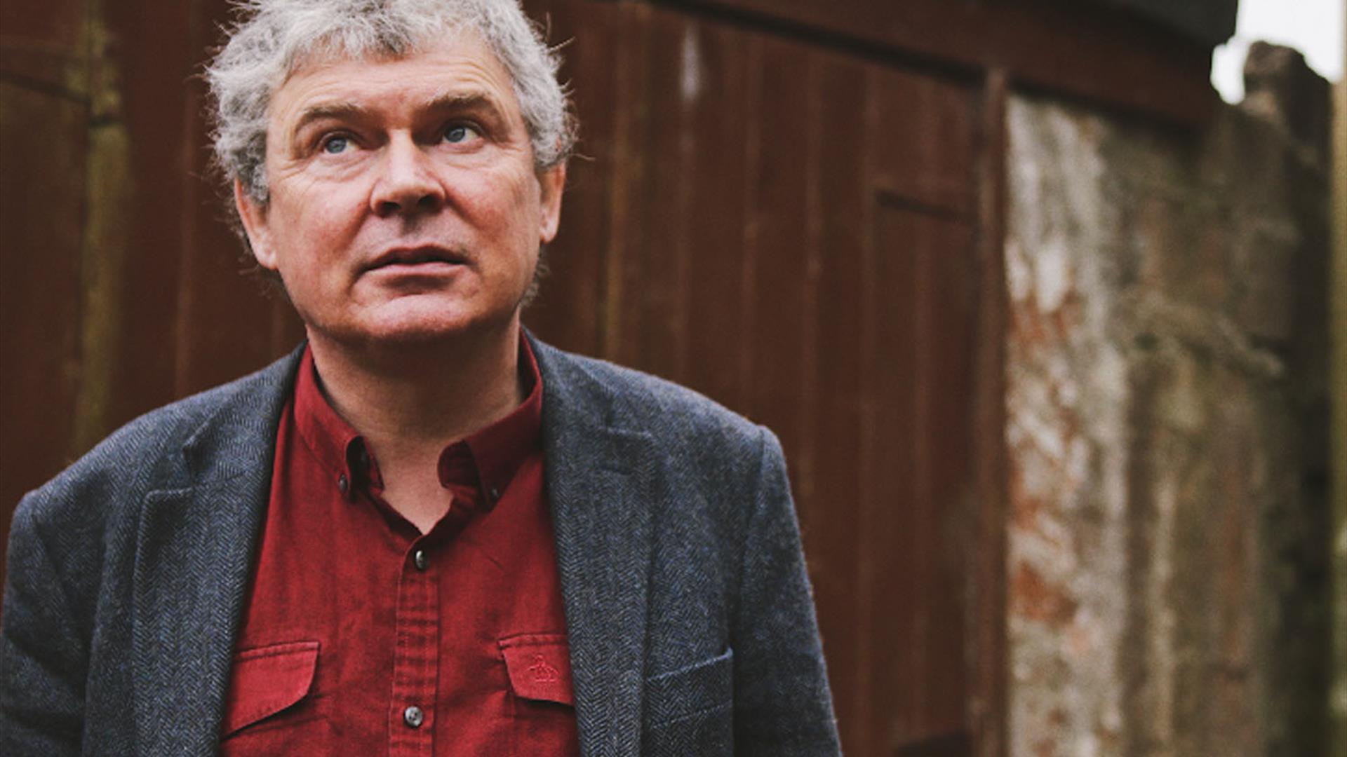 John Spillane stands infront of wooden garage doors, gazing towards the sky