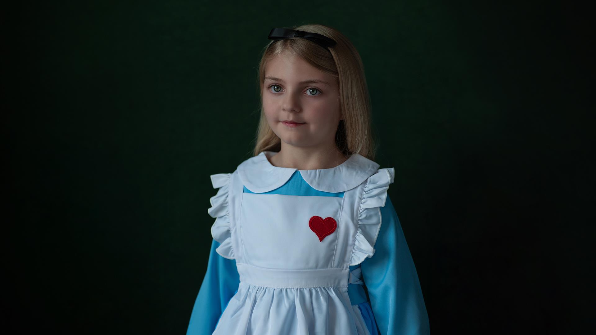 young child in blue dress with white apron and red heart broach