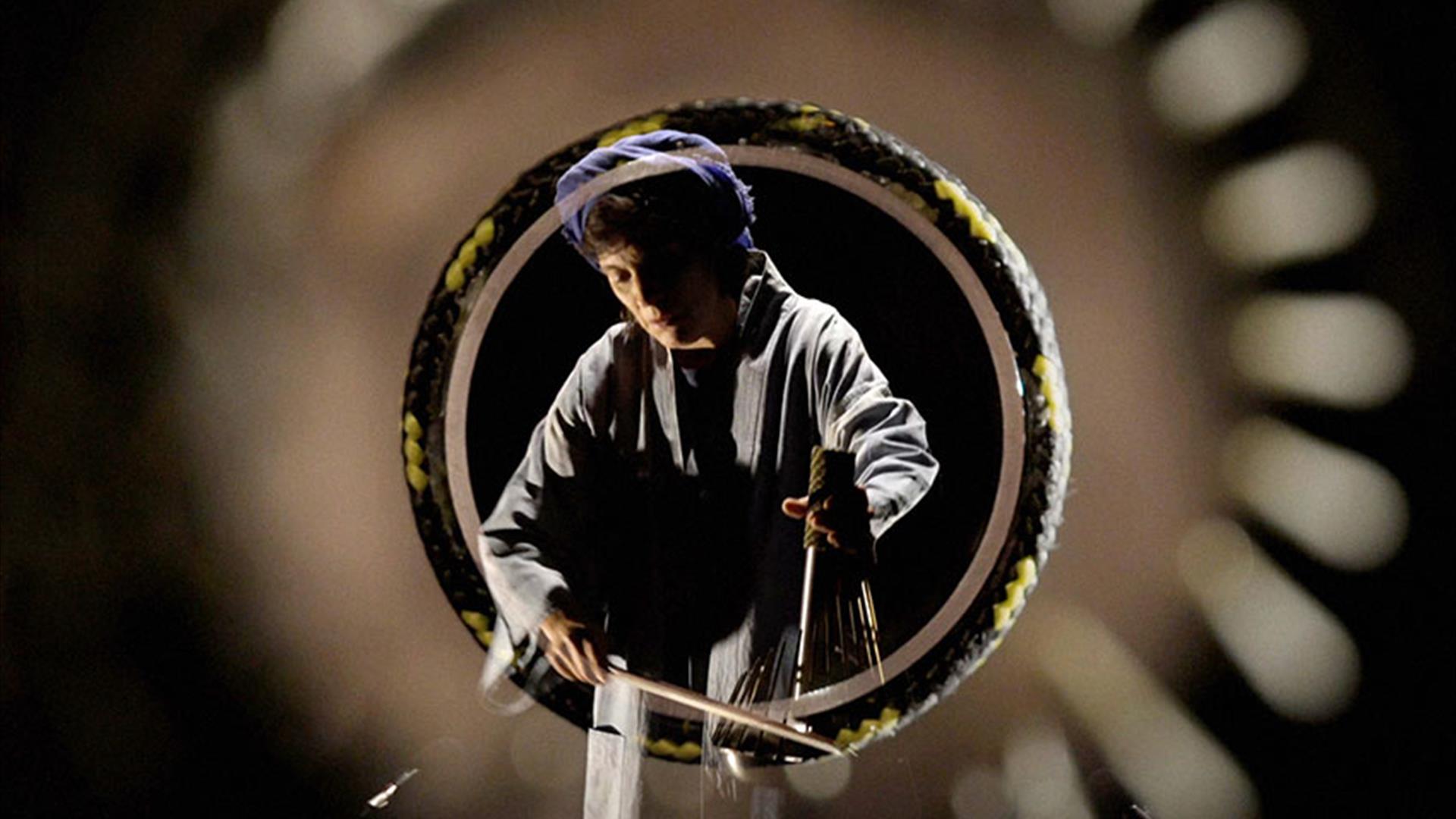 Person is surrounded by lens. They look downwards and there is a black background.