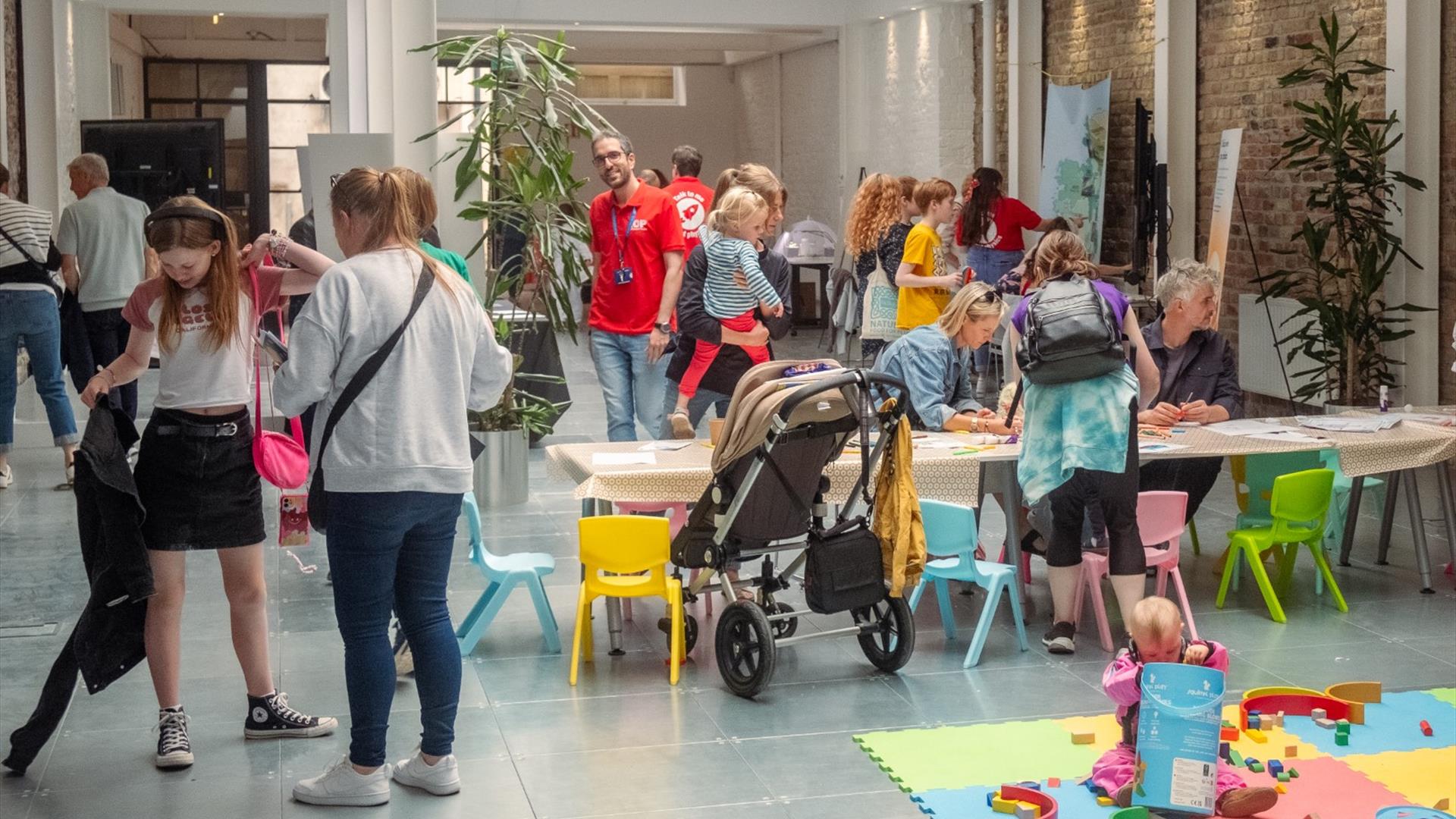 A busy indoor scene  of children and families drawing at a table in a gallery