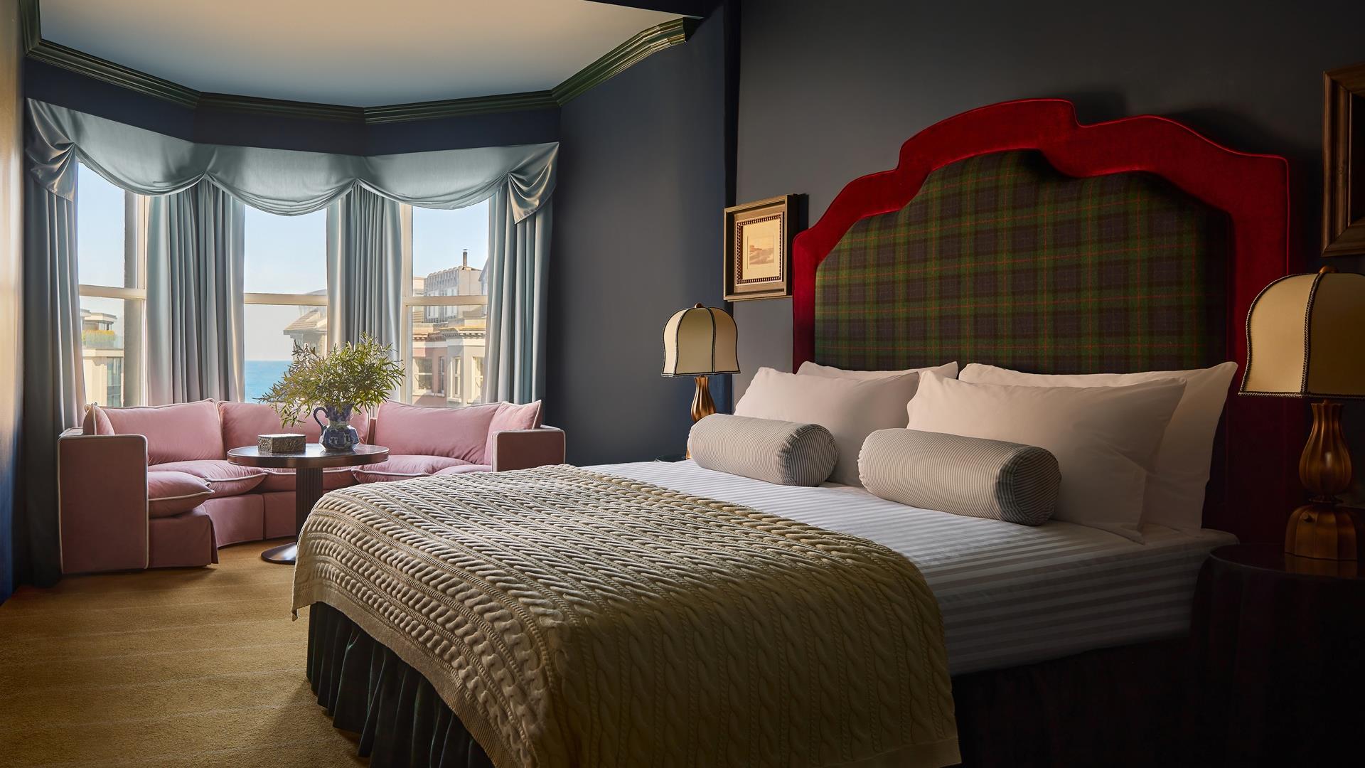 interior of double bedroom at Adelphi Hotel - features a tartan headboard and knitted throw on the bed, as well as a low pink sofa by the window overl
