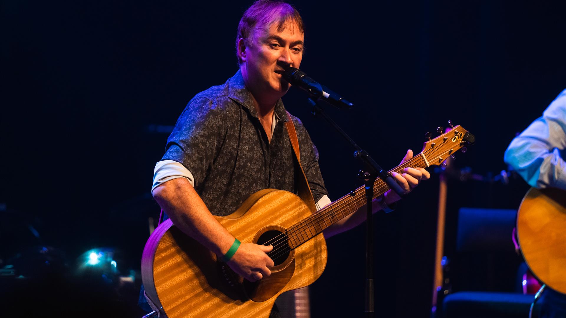 Image shows Brian standing, holding a guitar