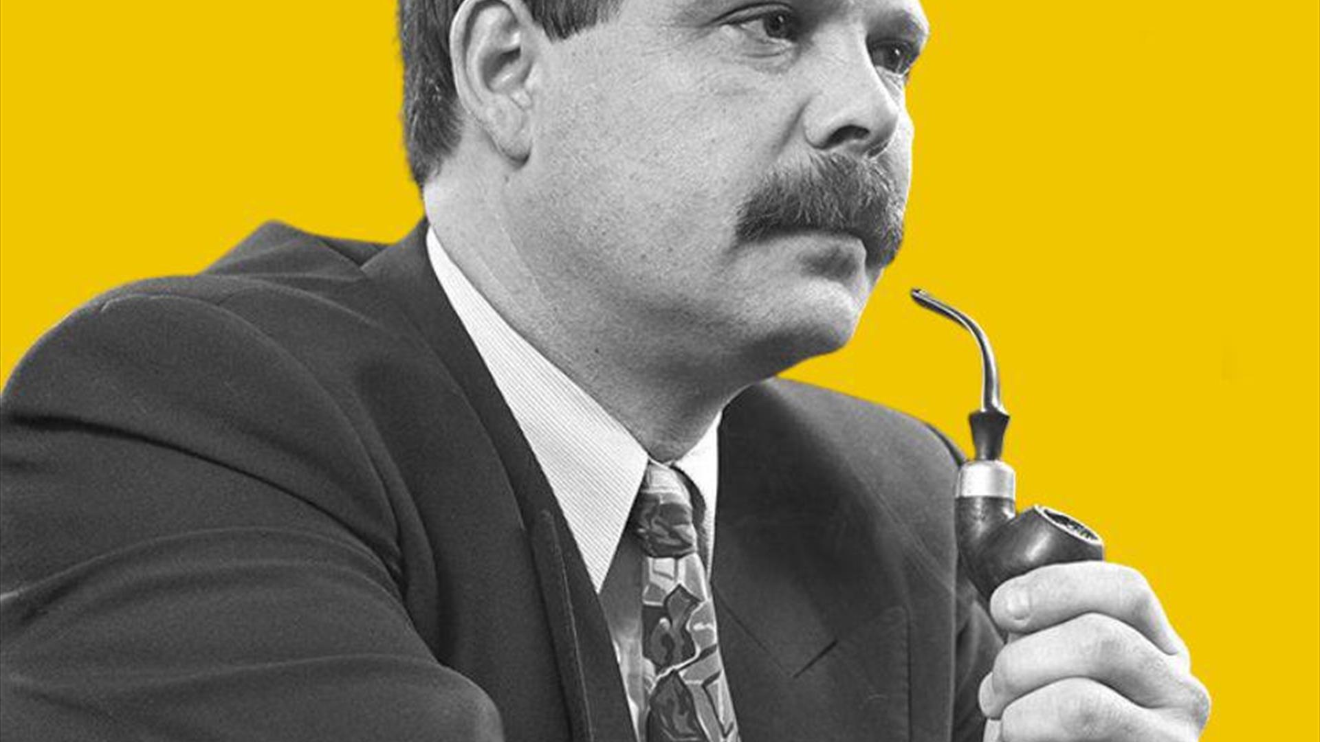 A man smokes a pipe in black in white colour saturation against a yellow background