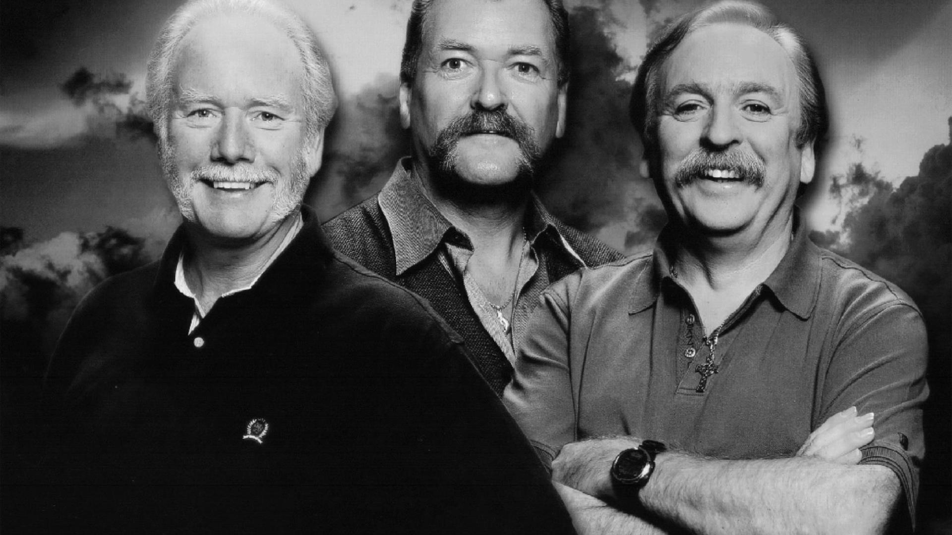 A black and white closeup  photo of The Wolfe Tones, smiling, with a dark, cloudy background