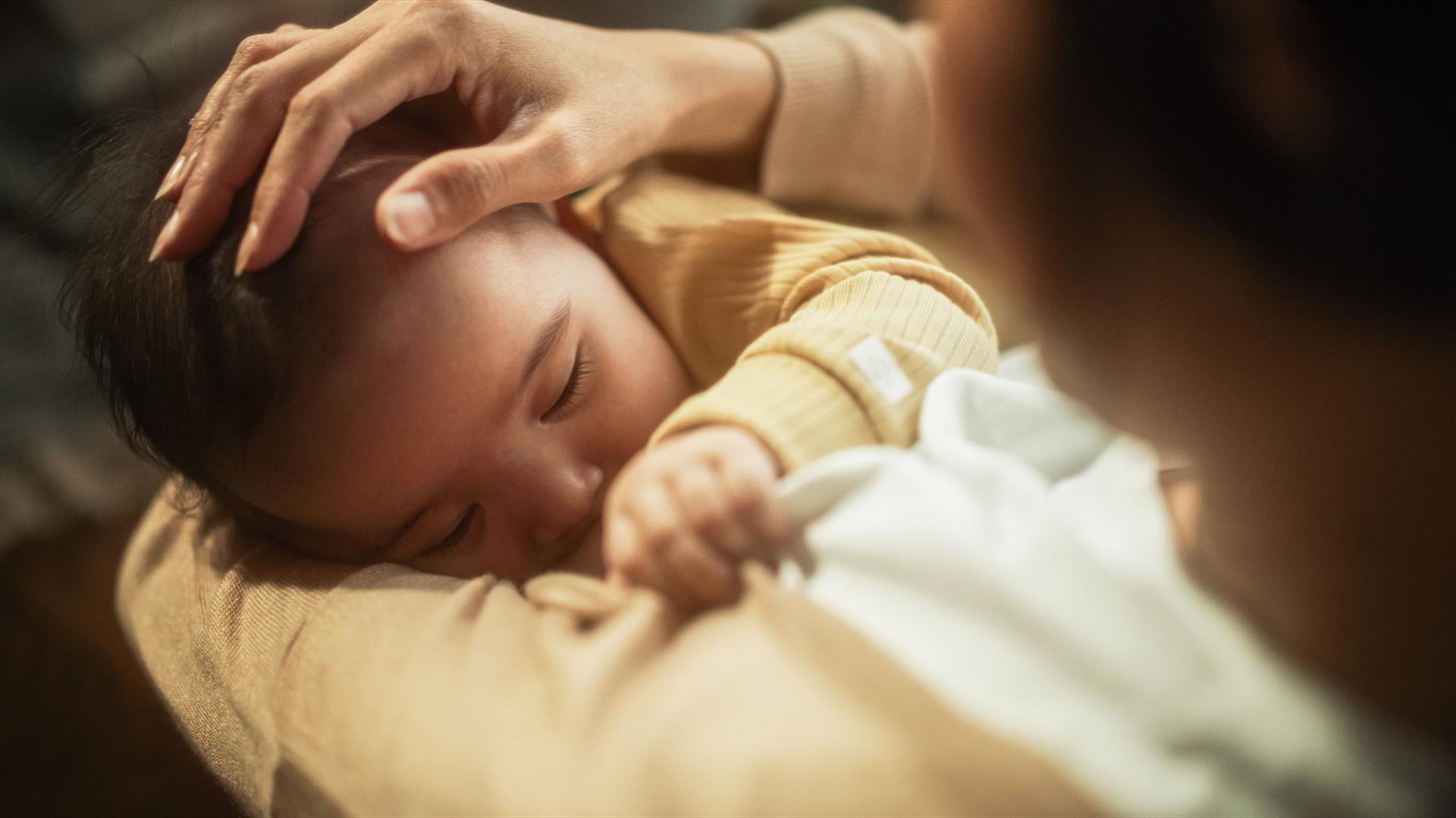 A mother looks down on her baby in her arms as she breastfeeds them.