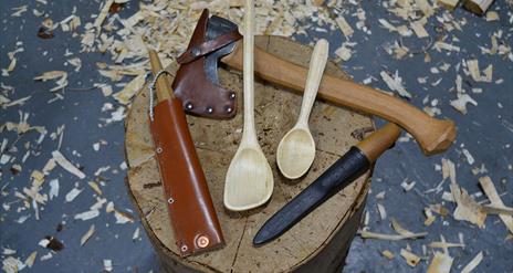 A photograph of wood-whittling tools and a carved spatula and spoon.