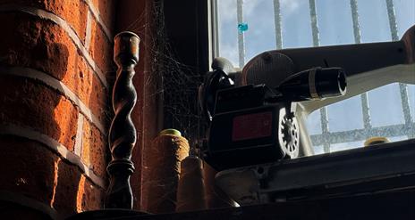 A candlestick and old sewing machine on a windowsill covered in cobwebs and dust.