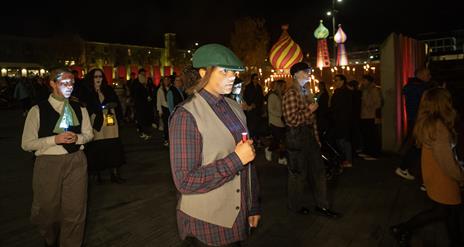 young girl dressed in old style clothing walking with a candle or light.