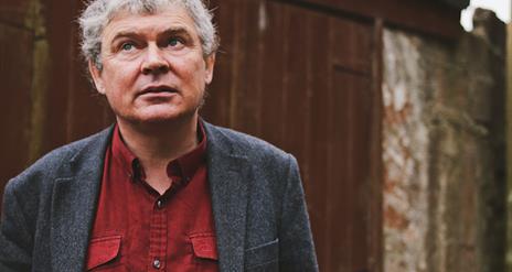 John Spillane stands infront of wooden garage doors, gazing towards the sky