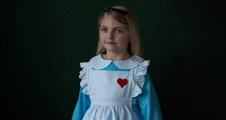 young child in blue dress with white apron and red heart broach