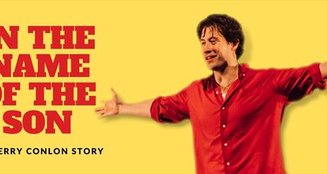 Actor playing Gerry Conlon stands in a red shirt with his arms open, smiling with triumph