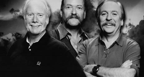 A black and white closeup  photo of The Wolfe Tones, smiling, with a dark, cloudy background