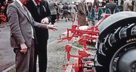 Two judges inspect farm equipment at a fair.