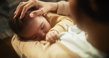 A mother looks down on her baby in her arms as she breastfeeds them.