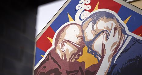 This is an image of a mural on a gable wall in Great James Street. The mural is of the Dalai Lama and Richard Moore. In the picture, their foreheads a