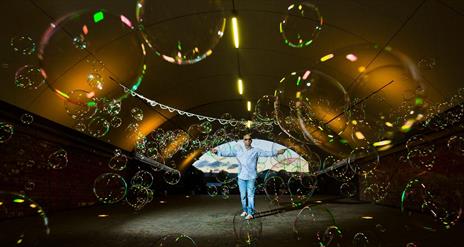 A man in sunglasses stands in a tent surrounded by hundreds of bubbles