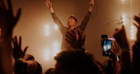 Ryan McMullan performing in front of a crowd, with his hands in the air, smiling