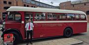 Vintage red and cream Derry City Bus Tours bus, driver/guide standing beside the entrance and a promotional sign at the front.