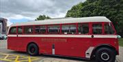 Vintage red and cream Derry City Bus Tours bus parked beside a pavement with trees and cloudy skies in the background.
