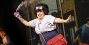 A lively character holding a can of hairspray joyfully sprays it into the air, wearing a retro outfit with a red handbag, set against a backdrop of 19