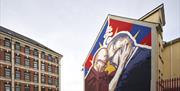 This is an image of a mural on a gable wall in Great James Street. The mural is of the Dalai Lama and Richard Moore. In the picture, their foreheads a