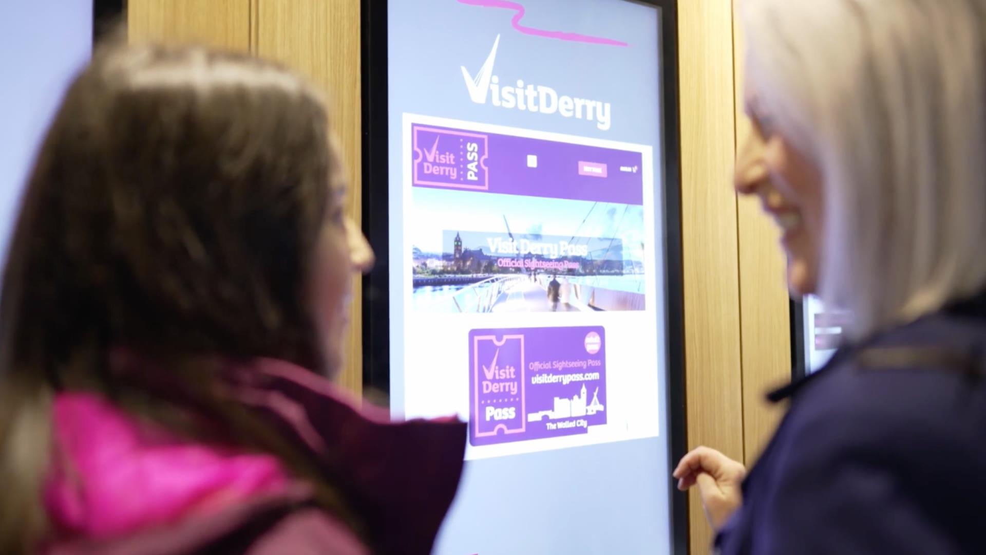 This  is an image of a mother and daughter buying the new sightseeing pass for Visit Derry in the Visit Derry Visitor Information Centre.