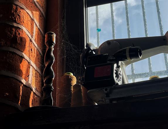 A candlestick and old sewing machine on a windowsill covered in cobwebs and dust.