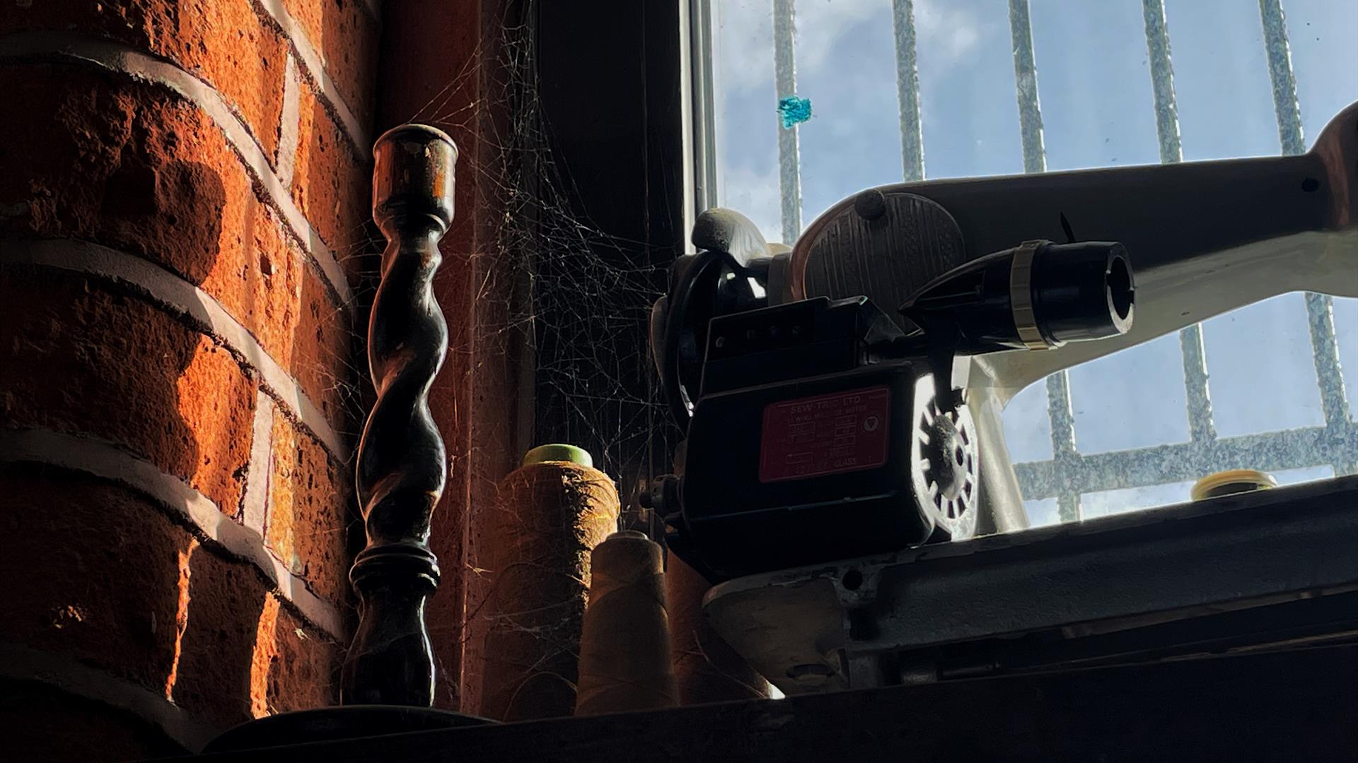 A candlestick and old sewing machine on a windowsill covered in cobwebs and dust.