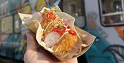 Fresh fish taco in the sunlight from Pyke N Pommes with their graffiti covered double decker bus in the background