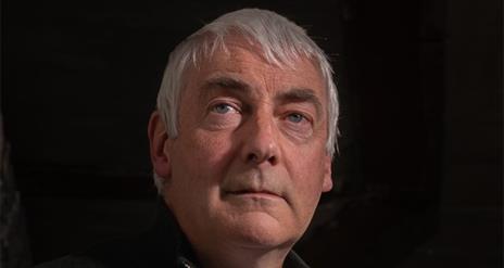 A close-up shot of Kevin McAleer against a black background, gazing vacantly beyond the camera lens.