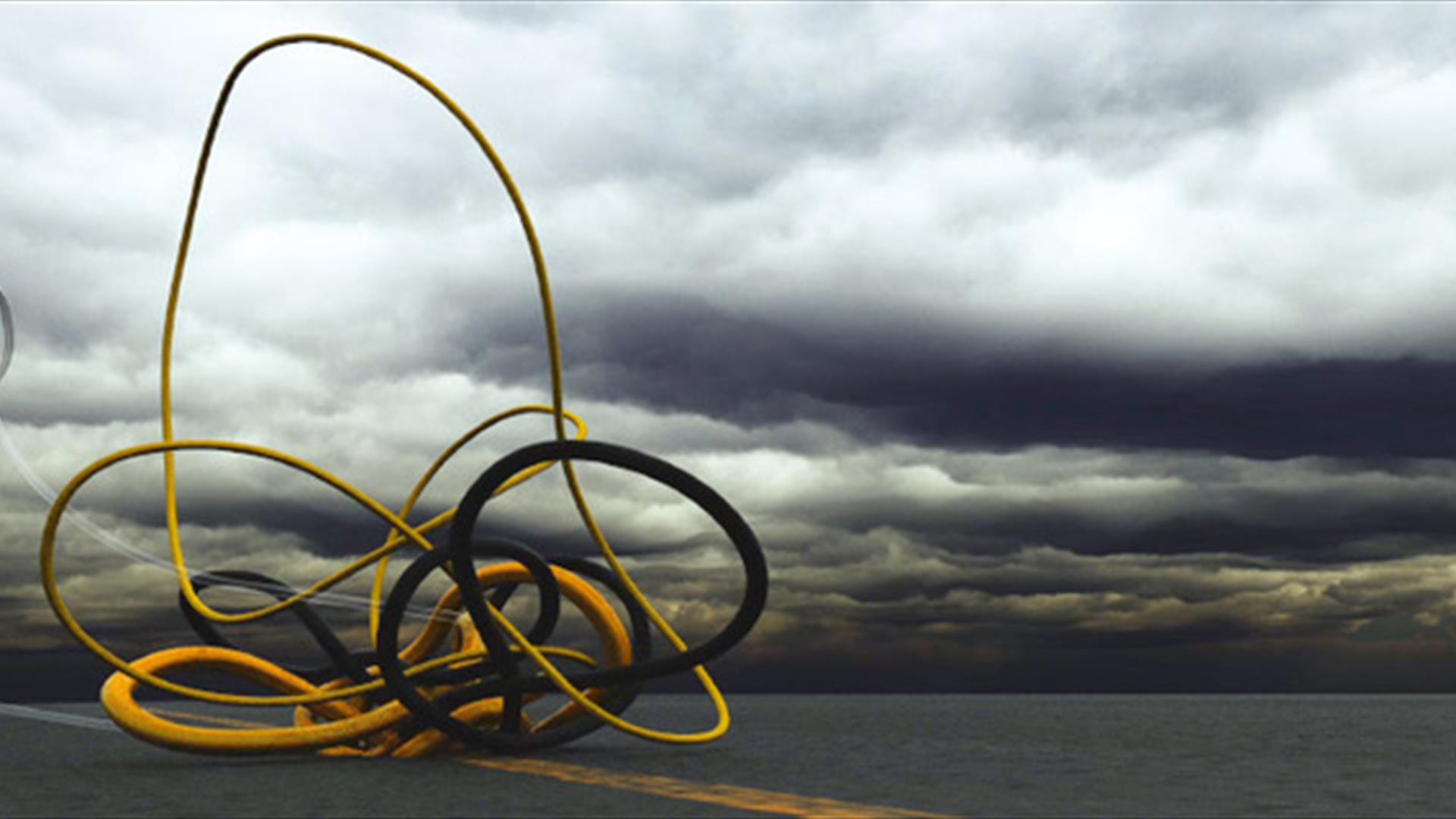 Grey cloudy stormy sky with hint of yellow sunset in the background. There are two pipes: yellow and black which are interweaved in the foreground.