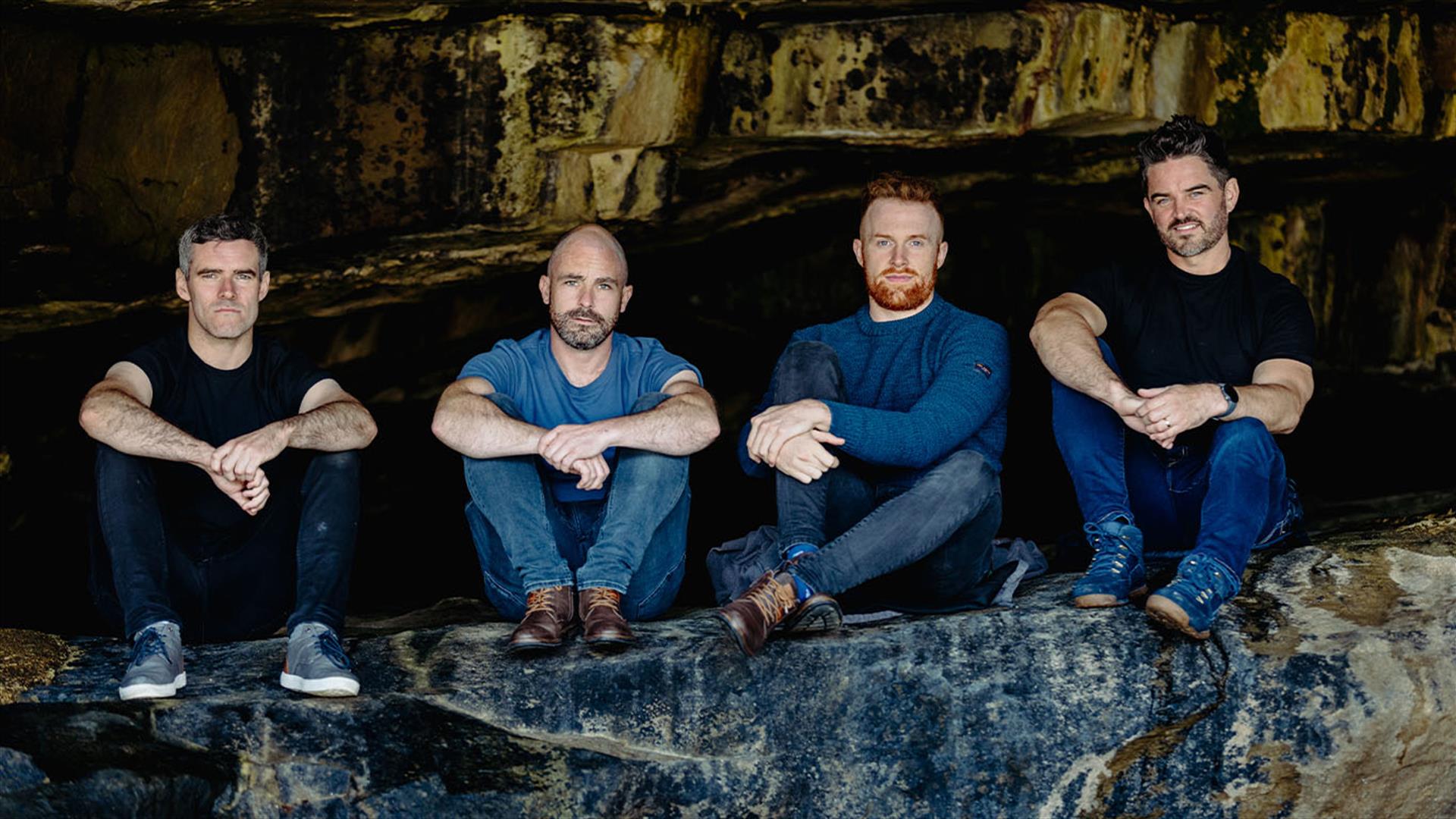 4 male band memebers sit in cave like surroundings
