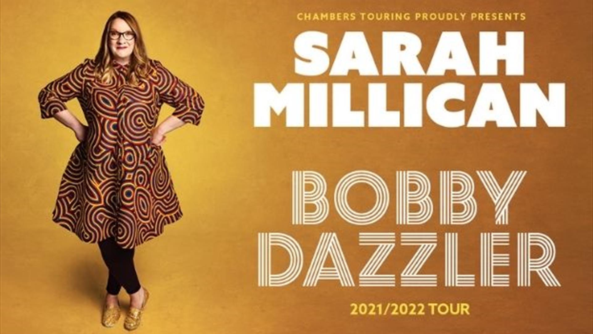Sarah Millican standing with her hands on her hips in a loudly patterned dress, beside her in large text- 'SARAH MILLICAN- BOBBY DAZZLER' against a wa