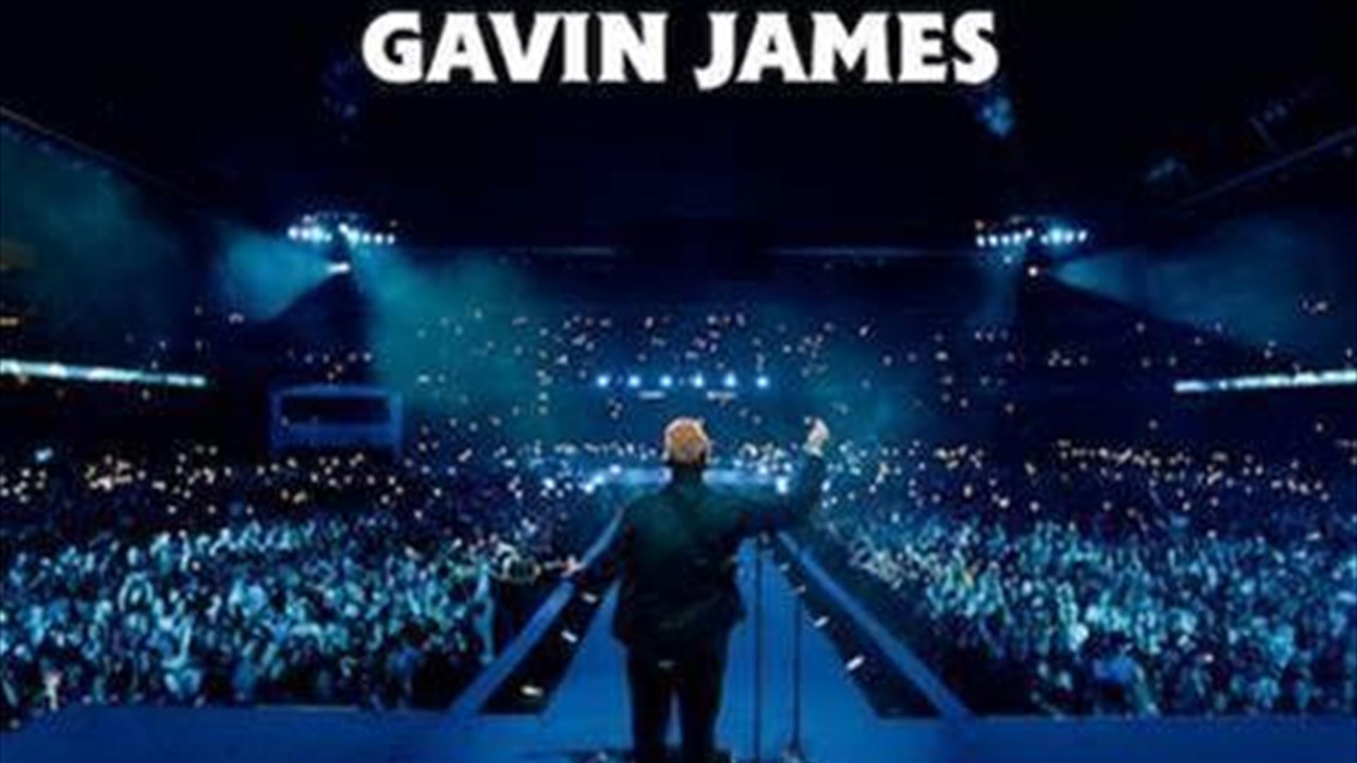 Gavin James facing a full arena, phone torches shining, blue mood lighting. White text above states 'Gavin James'.