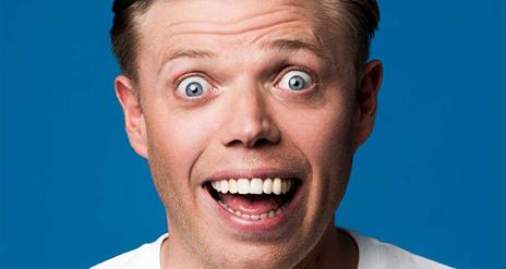 Rob Beckett Smiling widely in front of a deep blue background