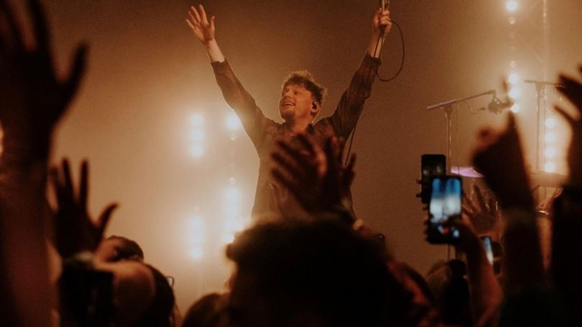 Ryan McMullan performing in front of a crowd, with his hands in the air, smiling