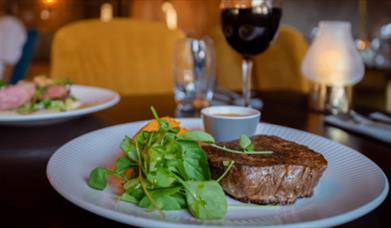 A plate of steak and a glass of wine at a restaurant.