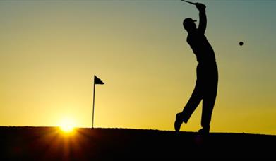 A man is playing golf as the sun sets