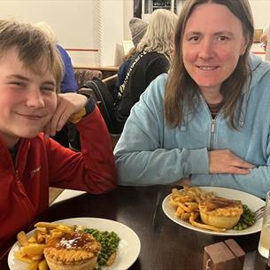 A woman and boy sitting at a table eating pie, chips and peas