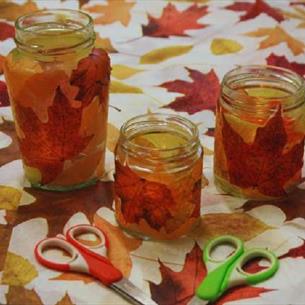 Leafy Lanterns at Ushaw. Jars with autumnal leaves in them, placed on a table with a leafy patterned tablecloth. 